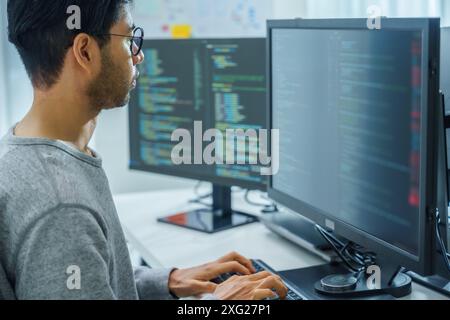 Der Prompt-Ingenieur des asiatischen Mannes entwickelt eine Codierungs-App mit Softwaredaten, die vor dem Computermonitor im Büro sitzen Stockfoto