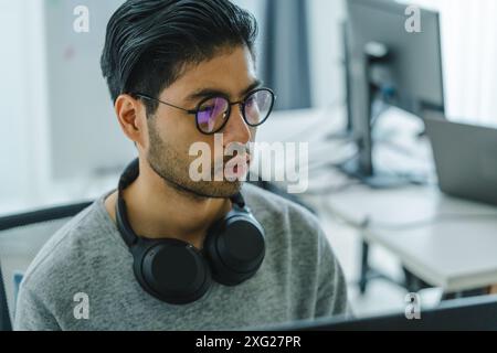 Der Prompt-Ingenieur des asiatischen Mannes entwickelt eine Codierungs-App mit Softwaredaten, die vor dem Computermonitor im Büro sitzen Stockfoto