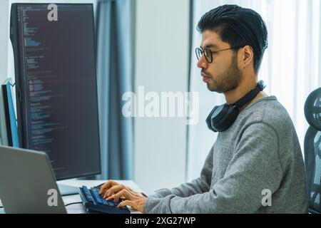 Der Prompt-Ingenieur des asiatischen Mannes entwickelt eine Codierungs-App mit Softwaredaten, die vor dem Computermonitor im Büro sitzen Stockfoto