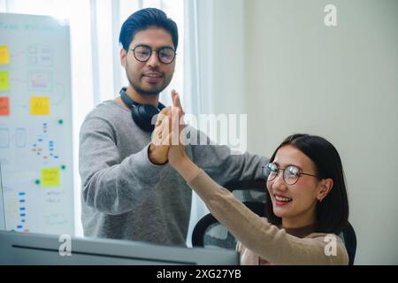 asiatische und indische Entwicklerteams klatschen Hand für Projekterfolg mit Software-Computer im Büro Stockfoto