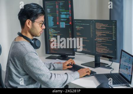 Der Prompt-Ingenieur des asiatischen Mannes entwickelt eine Codierungs-App mit Softwaredaten, die vor dem Computermonitor im Büro sitzen Stockfoto