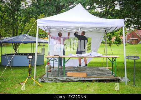 Zwei Männer von hinten, die einen Partypavillon für ein Sommerfest auf der Wiese in einem Park aufbauen, ausgewählter Fokus Stockfoto