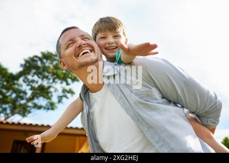 Vater, Kind und Huckepack im Garten für Spaß, Liebe und Bindung, um sich in der Kindheit zu Hause zu verbinden. Daddy, trage Sohn und Abenteuer Spiel für Flugzeug Stockfoto