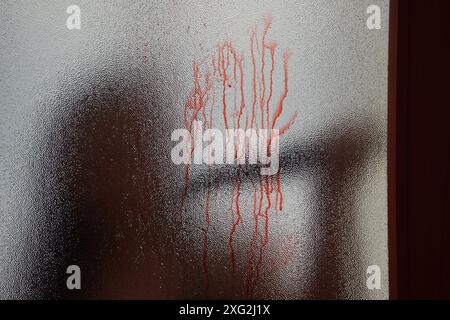 Geisterkonzeptschatten einer Frau hinter dem matten Glaskörper und Messer in der Hand. Blut auf dem Glas Stockfoto