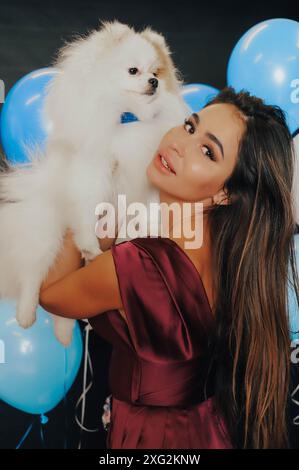 Die junge elegante Frau hält den kleinen Welpen sanft, Studioaufnahme, kleine Menge Körnung hinzugefügt Stockfoto