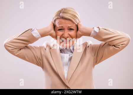 Bild einer frustrierten, reifen Geschäftsfrau, die ihre Ohren bedeckt und schreit. Stockfoto
