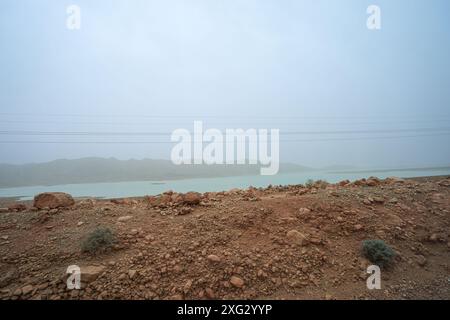 Panoramablick auf den Al-Wahda-Staudamm mit hoch aufragenden Stromleitungen und karger Vegetation. Al-Wahda-Staudamm, Fluss Ourgaha, Marokko. Stockfoto