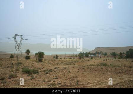 Panoramablick auf den Al-Wahda-Staudamm mit hoch aufragenden Stromleitungen und karger Vegetation. Al-Wahda-Staudamm, Fluss Ourgaha, Marokko. Stockfoto