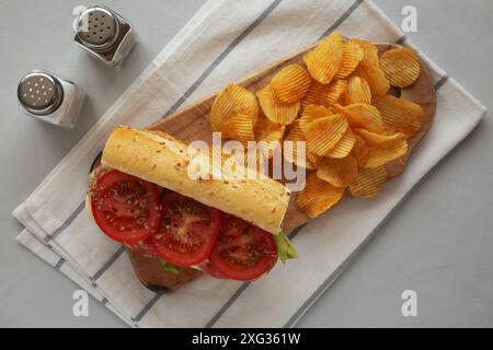 Hausgemachtes italienisches Sub-Sandwich mit Salami, Tomaten und geriebenem Eisbergsalat auf einem rustikalen Holzbrett, Blick von oben. Stockfoto