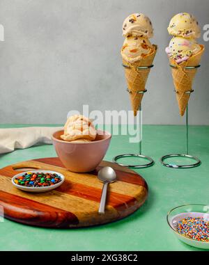 Ein wunderbares Arrangement von Eiskegeln und einer Schüssel Eis mit bunten Streuseln auf einem Holzbrett Stockfoto