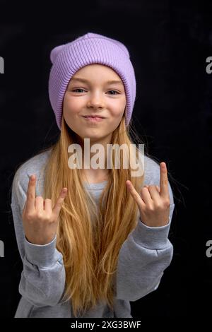 Porträt des lustigen coolen Teenager-Mädchens, das Rock Gesture macht, isoliert auf schwarzem Hintergrund. Ein wunderschöner junger kaukasischer Teenager, der die Hörner aufhebt. Glücklich Stockfoto