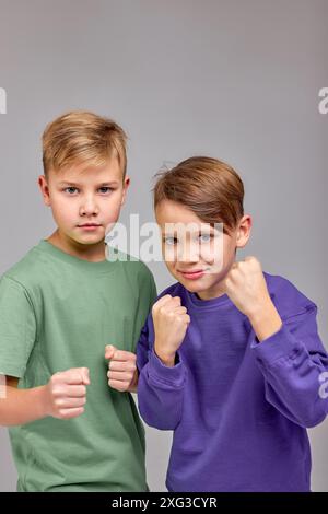 Porträt von kleinen kaukasischen Jungen, die vor dem Hintergrund der Wand stehen und grüne und blaue Pullover tragen und Kamerakinder anschauen, die Fäuste in f halten Stockfoto