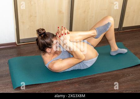 Aufnahme der Frau, die verschiedene Dehnungs- und körperliche Übungen durchführt und auf der Yogamatte auf dem Boden liegt Stockfoto