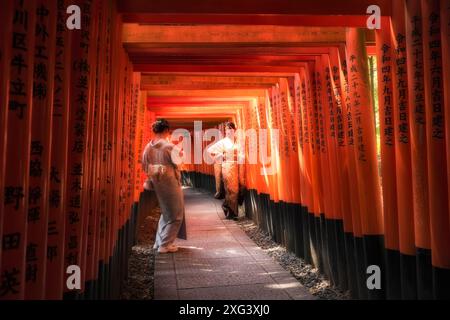 Kyoto, Japan – 19. Juni 2024: Zwei junge Frauen, die traditionelle japanische Kimonos tragen, fotografieren sich am Fushimi Inari Taisha Schrein und seinem Th Stockfoto