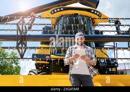 Ein Landarbeiter verwendet ein digitales Tablet, während er vor einem neuen Mähdrescher steht. Leasingvertrag, Händlerbetrieb für Landmaschinen Stockfoto