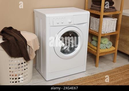 Waschmaschine, Korb und Regal in der Nähe beigefarbener Wände im Innenbereich Stockfoto