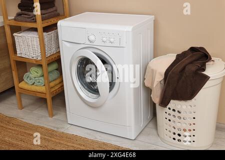 Waschmaschine, Korb und Regal in der Nähe beigefarbener Wände im Innenbereich Stockfoto