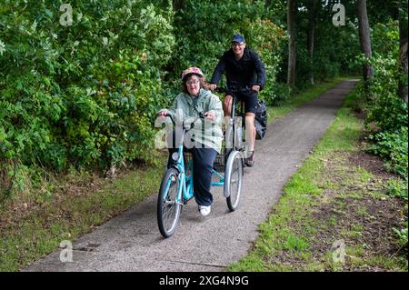 Meerhout, Antwerpen, Belgien - 1. August 2023 - 40 Jährige Frau mit dem Down-Syndrom, die mit ihrem Bruder im Wald das Dreirad fährt. Modell freigegeben Stockfoto