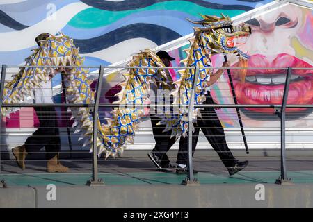 Darsteller tragen eine traditionelle chinesische Drachenpuppe mit einem farbenfrohen Wandgemälde im Hintergrund der Calgary Stampede Parade Stockfoto