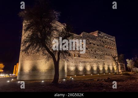 Jabreen Zitadelle Festung Steinmauern und runder Bastionturm in Nachtbeleuchtung mit Baum im Vordergrund, Bahla, Sultanat Oman Stockfoto