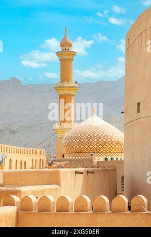 Al Qala'a Moschee mit reich verzierten Kuppel und Minarett mit den Mauern der Nizwa Burg im Vordergrund, Nizwa, Sultanat Oman Stockfoto