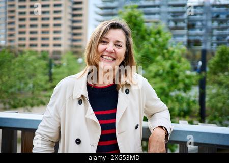Porträt einer fröhlichen Reifen blonden kaukasischen Frau, die glücklich steht und draußen auf Geländer gelehnt ist. Stockfoto