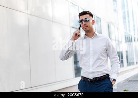 Ein Mann, der ein weißes Hemd trägt, ist in ein Telefongespräch verwickelt. Er hält ein Handy und mit freier Hand. Stockfoto