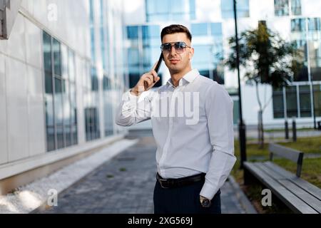 Ein Mann, der ein weißes Hemd trägt, wird gesehen, wie er ein Handy in der Hand hält. Der Mann scheint sich auf den Bildschirm des Geräts zu konzentrieren. Stockfoto