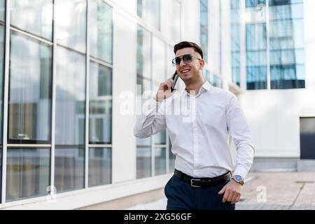 Ein Mann, der ein weißes Hemd trägt, führt ein Telefongespräch, während er ein Handy am Ohr hält. Stockfoto