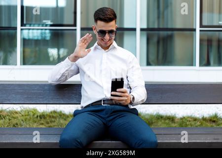 Ein Mann sitzt auf einer Bank, vertieft in sein Handy. Er scheint auf dem Bildschirm konzentriert zu sein, indem er den Inhalt eingibt oder durchblättert. Stockfoto