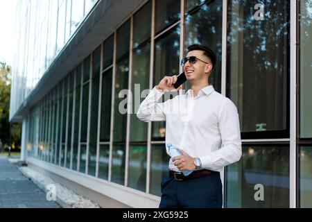 Ein Mann steht vor einem Gebäude und führt ein Telefongespräch. Er scheint sich auf den Ruf konzentriert zu sein, während er von urbaner Architektur umgeben ist Stockfoto