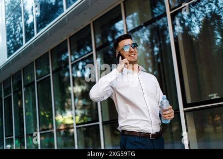 Ein Mann, der ein weißes Hemd und eine Sonnenbrille trägt, führt ein Telefongespräch. Er hält ein Handy am Ohr. Stockfoto
