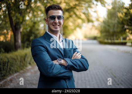 Ein Mann in Anzug und Sonnenbrille steht auf einer belebten Straße und blickt selbstbewusst nach vorne. Er scheint zu warten oder etwas zu beobachten. Stockfoto