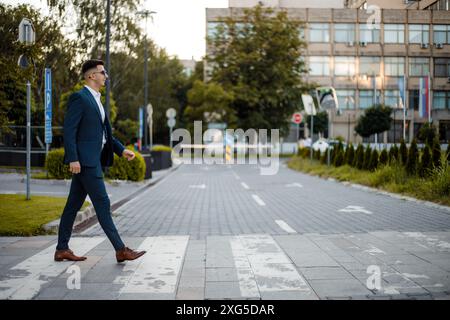 Ein Mann in einem formellen Anzug läuft über eine geschäftige Stadtstraße. Er scheint konzentriert zu sein. Stockfoto