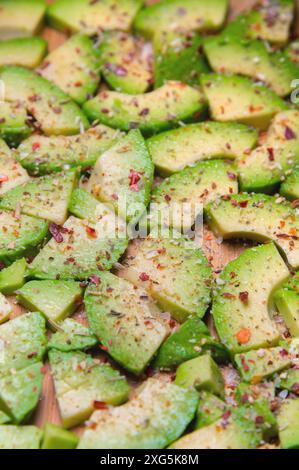 Große Scheiben reifer Avocado liegen strukturiert auf einem Holzschneidebrett. Mit Gewürzen bestreut. Gesunde Ernährung. Vegetarismus Stockfoto