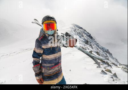 Porträt einer hübschen und aktiven Skifahrerin, die eine Maske trägt und Ski in der Hand hält, aktive Winterferien. Extreme Lifestyle-Konzept Stockfoto