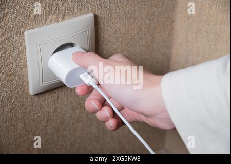 Weibliche Hand schaltet das Smartphone-Ladegerät über die Steckdose an der Wand ein oder aus, weiß Stockfoto