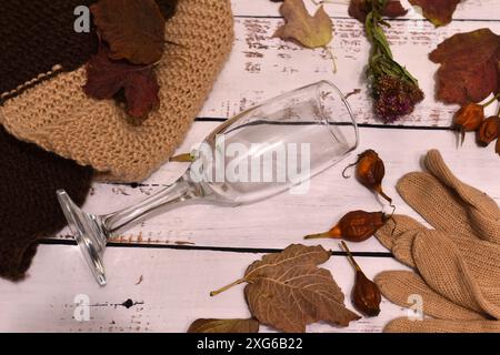 Herbstlandschaft. Auf dem Tisch stehen ein Schal, ein gefallenes Weinglas und gefallene gelbe Blätter. Stockfoto