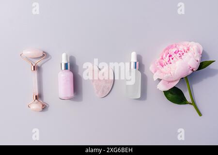 Zwei Kosmetikflaschen mit einer Pipette mit Öl oder Gesichtsmassage und Hautpflegeprodukt, einem Rollermassagegerät, einem Schaber auf grauem Hintergrund. Flache Lagen. Stockfoto