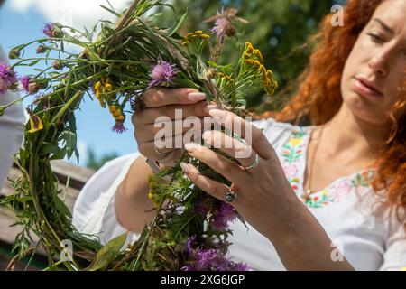 Moskau, Russland. Juli 2024. Eine Frau webt einen Kranz aus Wildblumen während einer Feier des belarussischen Feiertags „Kupalle“ im Ostankino-Park in Moskau, Russland. Kupalle oder Ivana Kupala Day, auch bekannt als Ivana-Kupala oder Kupala Night, ist eine traditionelle heidnische Feiertagsfeier in ostslawischen Kulturen. Mädchen kreieren und tragen Blumenkränze und führen verschiedene Rituale aus. Anfangs war Ivana-Kupala ein heidnischer Fruchtbarkeitsritus, der auch mit der Feier der Sommersonnenwende verbunden war, wenn die Nächte am kürzesten sind Stockfoto