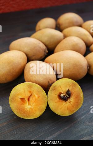 Nahaufnahme der geschnittenen Sapodilla-Frucht mit Haufen ganzer Früchte im Hintergrund Stockfoto