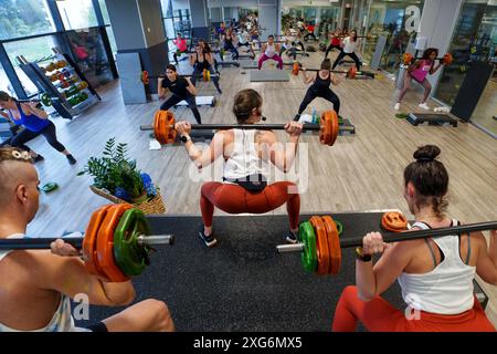 Fitnesslehrer, die während des Les Mills Body Pump Fitnesskurses im Fitnessstudio Squats machen Stockfoto