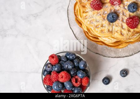 Blick von oben auf belgische Waffeln und eine Mischung aus Himbeeren und Heidelbeeren auf Marmorhintergrund. Köstliches Sommerfrühstück. Stapel hausgemachte runde Waffeln Stockfoto