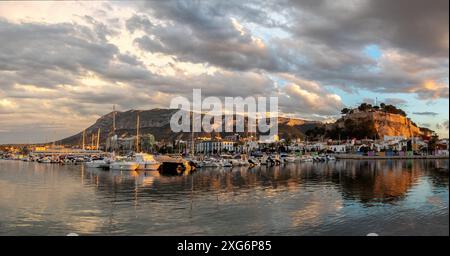 Ein Panoramablick auf Denia, Spaniens Uferpromenade, zeigt den Jachthafen, die Burg und den Montgo Naturpark, während die untergehende Sonne die Szene in goldenes Licht taucht. Stockfoto