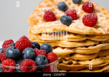 Nahaufnahme von gemischten Himbeeren und Heidelbeeren und belgischen Waffeln im Hintergrund. Gesundes, leckeres Sommerfrühstück mit Obst. Stapel hausgemachte Runde Stockfoto