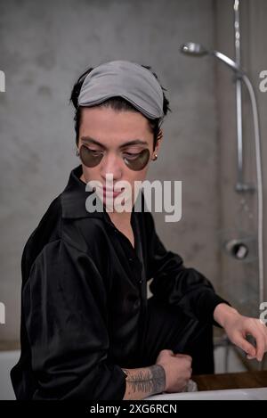 Der junge Mann führt einen glamourösen Lebensstil. Ein attraktiver brünette Mann in einem eleganten schwarzen Bademantel, der luxuriöse Badezimmermode trägt. Stockfoto