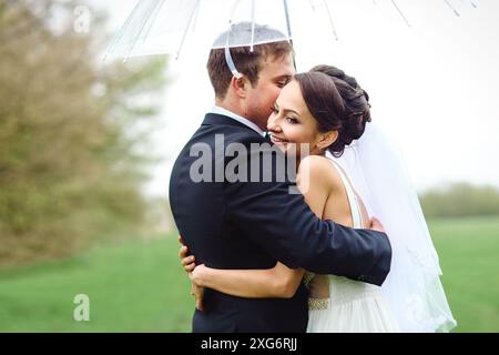 Braut und Bräutigam an einem regnerischen Hochzeitstag, der unter einem Regenschirm läuft Stockfoto
