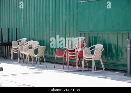 An sonnigen Tagen stehen neben der Terrasse des Cafés weiße und rote Plastikstühle. Detaillierte Darstellung des Musterstapels von Kunststoffstühlen, Platz für Text Stockfoto