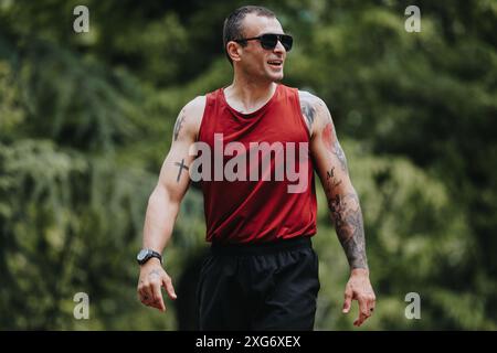 Sportlicher Mann in rotem Tanktop mit Tattoos, der Outdoor-Workout genießt Stockfoto