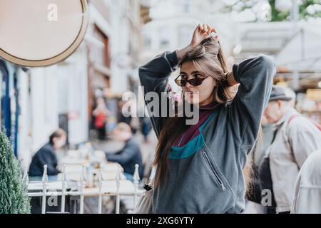 Eine junge Frau, die die Haare justiert, während sie die Straßen einer belebten Stadt erkundet Stockfoto